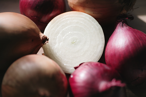 Woman picking red onions. Fresh whole purple onions and one sliced onion on a wooden countertop