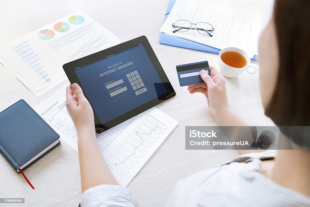 Online internet banking Successful businesswoman sitting at desk in casual clothes and inputting her password and login to carry out online banking operation on digital tablet in the office Bank Account Stock Photo