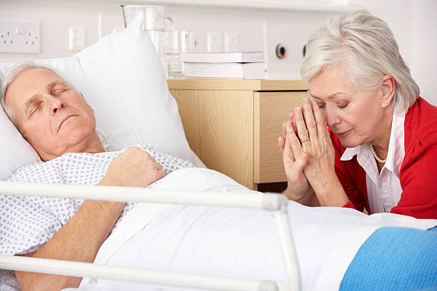 Senior woman with seriously ill husband in hospital Senior woman with seriously ill husband in hospital praying by bedside nervous holding hands stock pictures, royalty-free photos & images