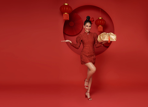 Happy smiling Asian woman in red traditional costume giving gold gift box on decoration traditional for chinese new year header copy space background.