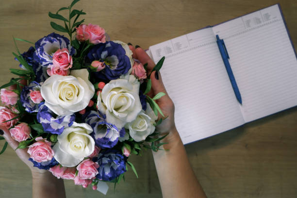 istock Flatlay. Female hands hold a bouquet of multi-colored roses flower. Notebook, diary with a pen on a wooden table 1784006019