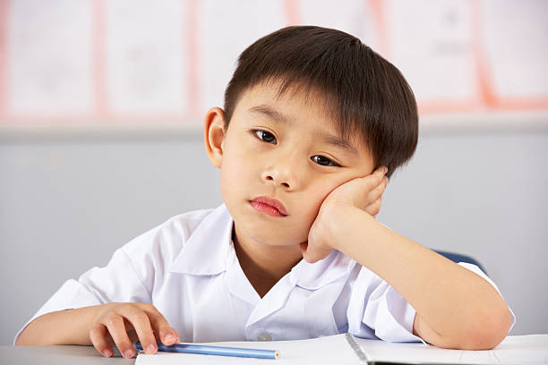 infeliz homem aluno a trabalhar na mesa em escola chinesa na sala de aulas - learning boredom studying child imagens e fotografias de stock