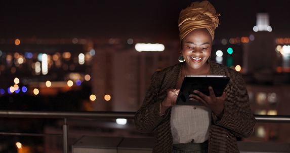 Tablet, night and balcony with a business black woman doing research online while standing outdoor at her office. Working late, search and deadlines with a female employee doing overtime at work
