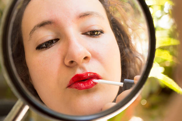 istock young woman applying ​​lipstick using a rearview mirror 178402174