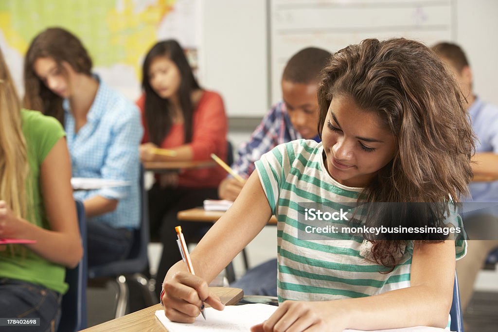Female Pupil Studying At Desk In Classroom Female Pupil Studying At Desk In Classroom Sitting At Desk Writing In Textbook Educational Exam Stock Photo