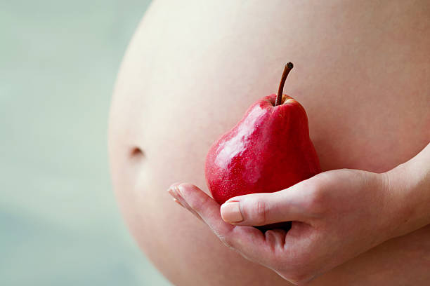 asian pregnant woman sitting on sofa with apple, orange,  in her hands close up selective focus.