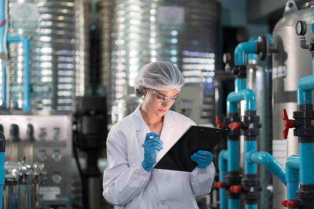 lavoratrice che indossa l'uniforme, lavoro a rete per capelli e controllo del sistema di pompaggio dell'acqua, stazione di tubazioni, sistema di pressione dell'acqua, serbatoio dell'acqua alla linea di produzione nella fabbrica industriale - chimico foto e immagini stock