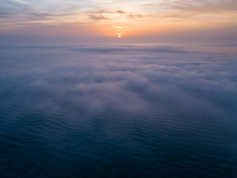Aerial view of a sunrise sea with a blanket of morning fog and morning sunbeams shining through.