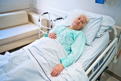 Thoughtful senior woman lying on bed in hospital.