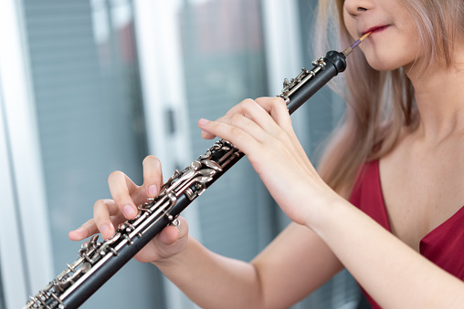 Beautiful young woman in a red dress playing the clarinet \n,Classical musician oboe playing.