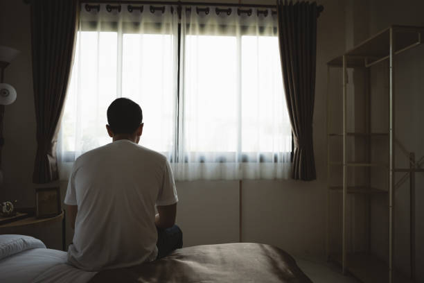 silhouette deprimierter mann, der traurig auf dem bett im schlafzimmer sitzt. traurige asiatische männer, die an depressionen und schlaflosigkeit leiden, wachen auf und sitzen allein auf dem bett im schlafzimmer. depression gesundheit menschen konzept. - einsamkeit stock-fotos und bilder