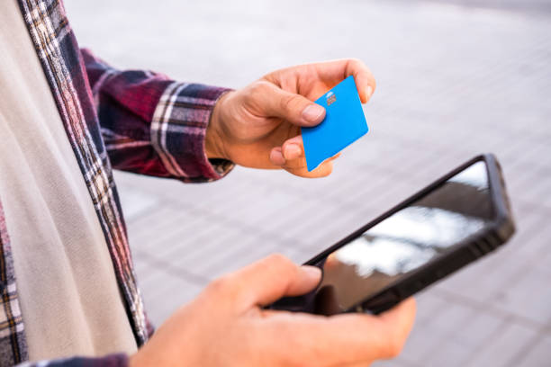 Young man uses his bank card and smartphone to make online purchases from a city street. stock photo