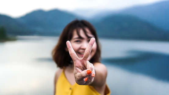 Happy smiling asian woman showing victory sign. concept of enjoyment, weekend holidays and traveling and standing. Blur focus background outdoor. Photo of lovely woman show v sign.