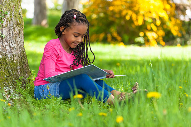 Cute young black little girl reading a book Outdoor portrait of a cute young black little  girl reading a book - African people little black girl hairstyle stock pictures, royalty-free photos & images