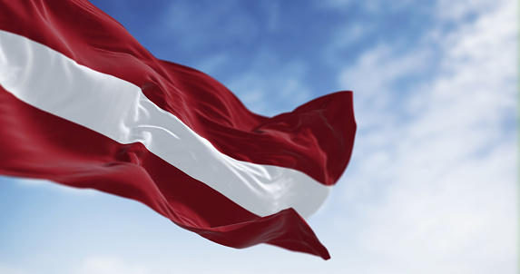 Republic of Latvia national flag waving in the wind on a clear day. Red field with a white horizontal line in the middle. 3d illustration render. Rippling fabric. Selective focus. Waving flag