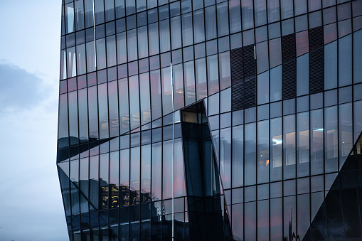 This captivating image showcases a modern business building adorned with a sleek glass facade, standing proudly in the enchanting dawn blue light. The gentle, cool hues of the early morning sky cast a soft and serene glow upon the structure, creating an atmosphere of tranquility and sophistication. The building's reflective glass exterior mirrors the surrounding environment, creating a mesmerizing interplay of light and reflections. This image serves as a stunning abstract background, exuding a sense of contemporary elegance and professional allure, making it ideal for a wide range of design and business applications. Copy space.