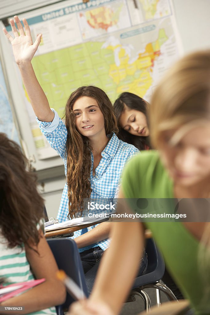 A female student answering a question in class Female Pupil Answering Question In Classroom Sitting At Desk High School Student Stock Photo