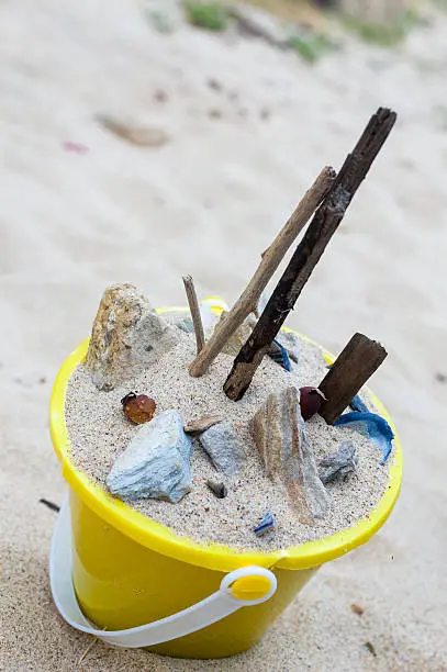Photo of Yellow bucket of beach sand, rocks, shells and sticks