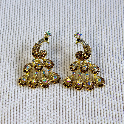 Golden handmade earrings on tinsel on grey textured fabric background close up