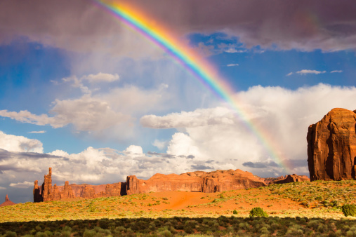 A brilliant rainbow arcs above sandstone monoliths in Monument Valley, an iconic natural landscape in the American Southwest.