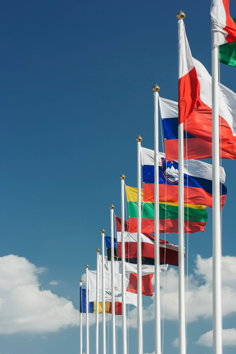 national flags of Europe and other countries on satin flutter in wind in blue sky near building of European Parliament, state symbols, concept of international cooperation, global business