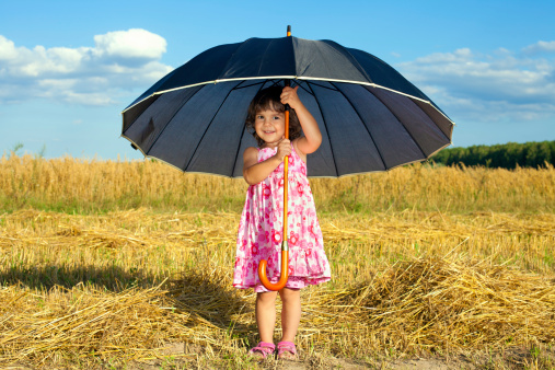 Happy little girl hiding under big black umbrella in fair weather