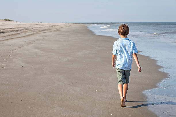 enfant marchant le long de la plage - shorts rear view summer beach photos et images de collection