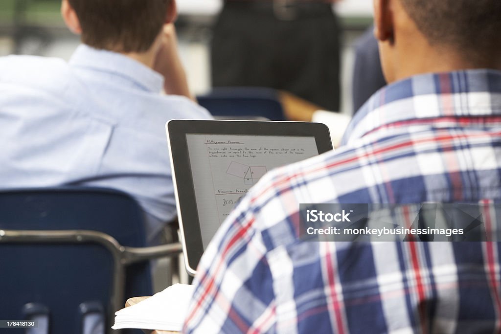 Male Pupil Using Digital Tablet In Classroom Male Pupil Using Digital Tablet In Classroom Sitting At Desk Digital Tablet Stock Photo