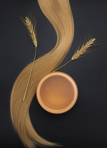Blond long hair with cream jar and sprigs of ripe wheat. Healthy hair. Black background. Hair tools, beauty and hairdressing concept. Hair care, healthy hair.