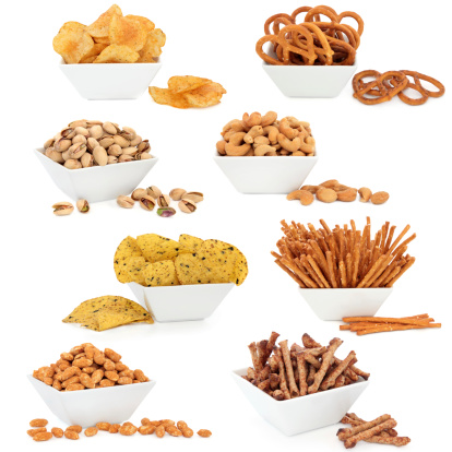 Crisps, tortillas, nuts and pretzel snack food selection in porcelain dishes over white background.