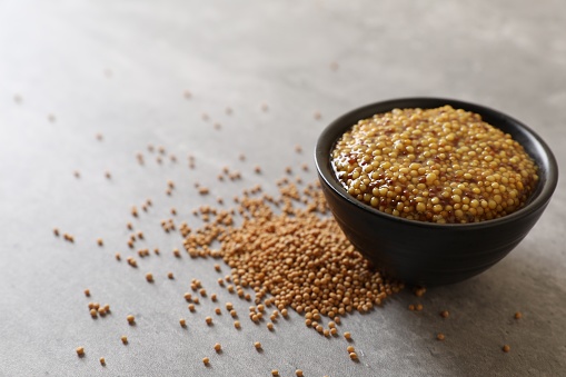 Bowl of whole grain mustard and seeds on grey table