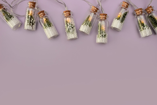 lilac background with unusual creative Christmas lights on the top, in the form of a glass bottle inside the fir tree and snow. copy space, flat lay