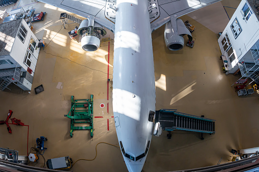 Top view of a white passenger airliner in the aviation hangar. Aircraft under maintenance. Checking mechanical systems for flight operations