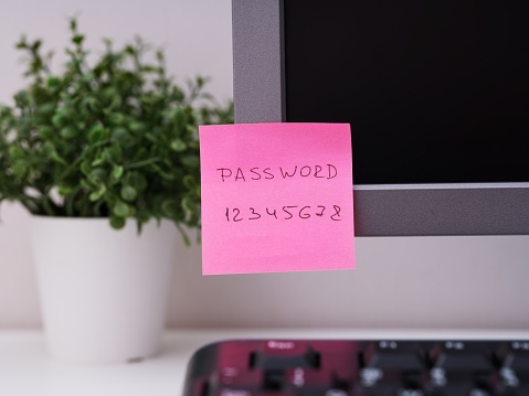 A pink paper note with the reminder Password 12345678 on it sticked on to a monitor at an office workplace.