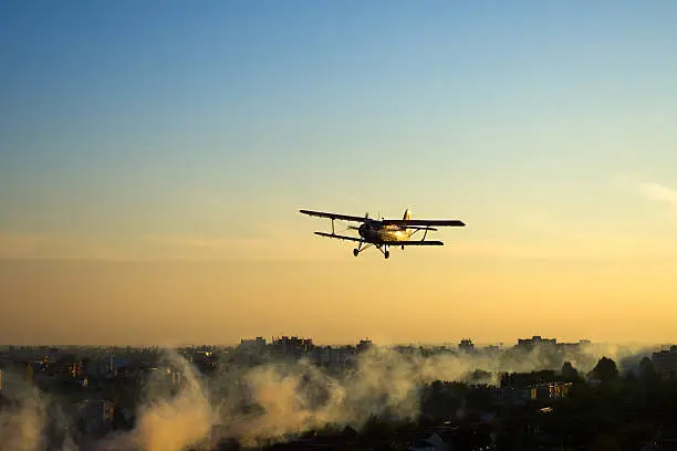 Red vintage biplane sprays mosquitoes over European town of Osijek, Croatia.