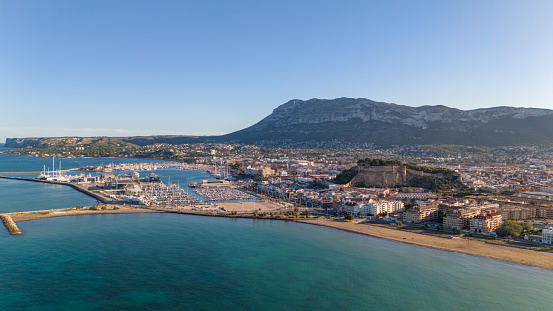 This aerial drone photo shows the coastal town of Denia in the Costa Blanca, Spain. There is a large marina in the town with a ferry terminal. Also you can find a beautiful boulevard and the sea is crystal clear.