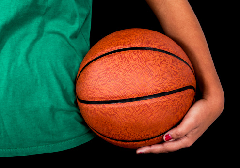 Close-up of a basketball with woman holding it. Studio shot with black background