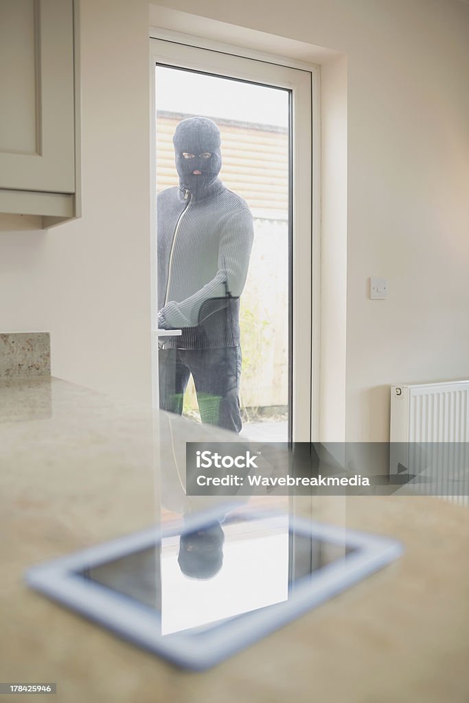 Ladrón de casas looking at tablet pc a través de la puerta de la cocina - Foto de stock de Abrir libre de derechos