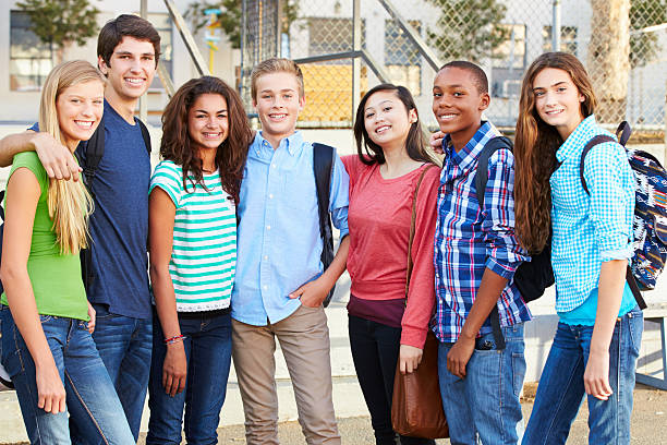 Group Of Teenage Pupils Outside Classroom Group Of Teenage Pupils Outside Classroom With Arms Round Each Other Smiling At Camera schoolyard photos stock pictures, royalty-free photos & images
