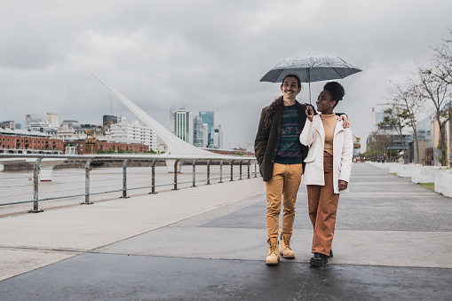 Young couple walking using umbrella in Puerto Madero, Buenos Aires