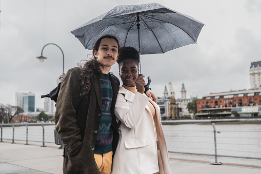 Portrait of a young couple walking using umbrella in Puerto Madero, Buenos Aires