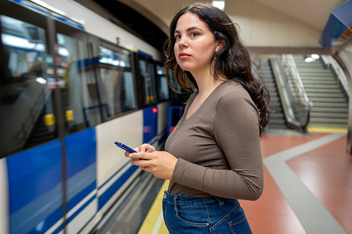 Side view of a young female commuter using mobile phone in the subway station