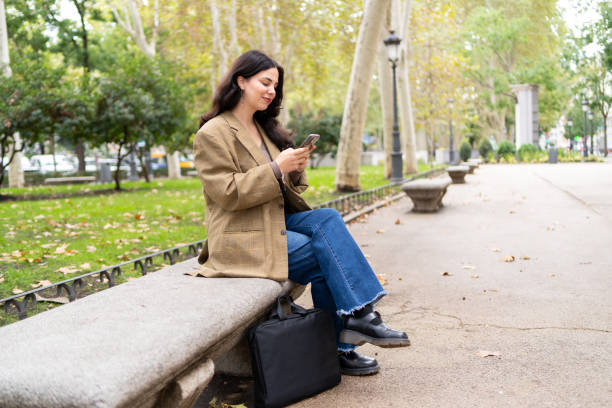 istock Casual businesswoman using phone sitting on a park bench 1784279420
