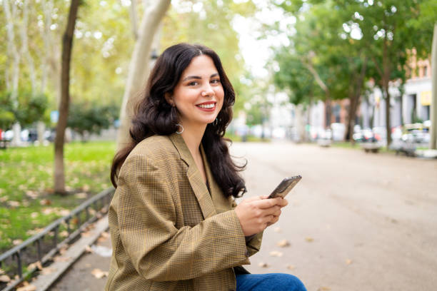 istock Smiling businesswoman using phone sitting on a park bench 1784279432