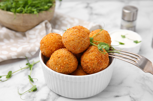 Bowl of delicious fried tofu balls with pea sprouts on white marble table