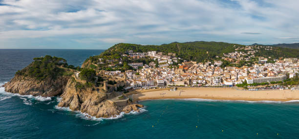 This aerial drone photo shows a panorama of the coastal town named Tossa de Mar. Tossa de Mar is located at the Costa Brava in Catalonia, Spain. There is a castle on the rocks and a beautiful beach.