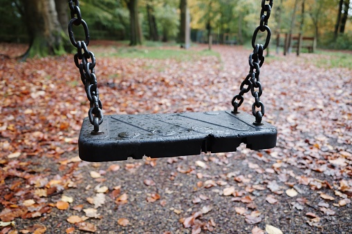 closeup of child's swing seat and metal chains in the park under the trees