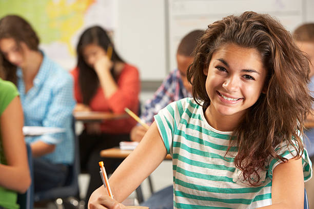 Portrait Of Female Pupil Studying At Desk In Classroom Portrait Of Female Pupil Studying At Desk In Classroom Smiling At Camera boy and girl looking at camera stock pictures, royalty-free photos & images