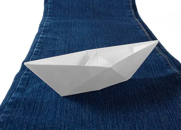A paper boat sailing on a blue stream made of a pair of blue jeans
