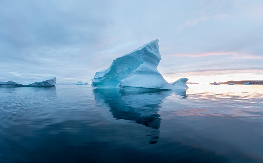 Arctic nature landscape with icebergs in Greenland icefjord with midnight sun. Early morning summer alpenglow during midnight season. Tip of the iceberg.
